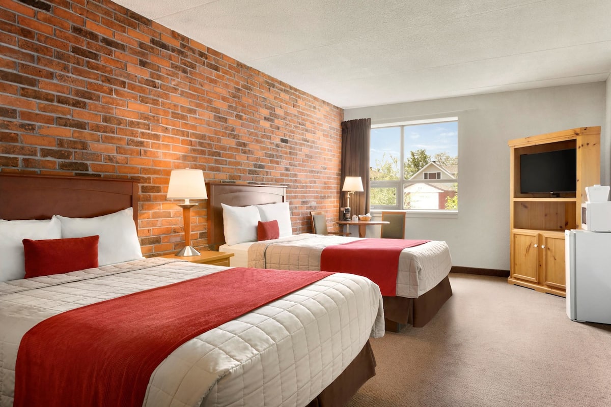 A hotel room with two beds, a brick wall, a window with a view, a TV cabinet, and a refrigerator.