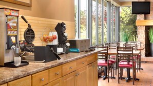 Un restaurante con zona de cocina, una máquina de café, un fabricante de gofres y un televisor montado en la pared.