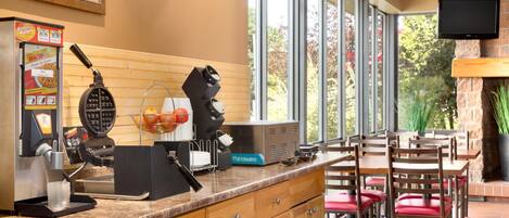 A restaurant with a kitchen area, a coffee machine, a waffle maker, and a television mounted on the wall.