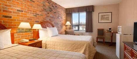A hotel room with two beds, a brick wall, a window with curtains, a desk with a computer, and a television.