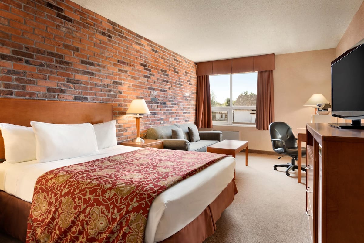 A hotel room with a large bed, a desk, a chair, and a TV.