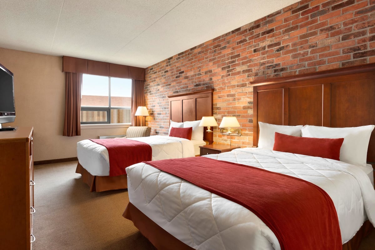 A hotel room with two beds, a brick wall, and a television on a dresser.