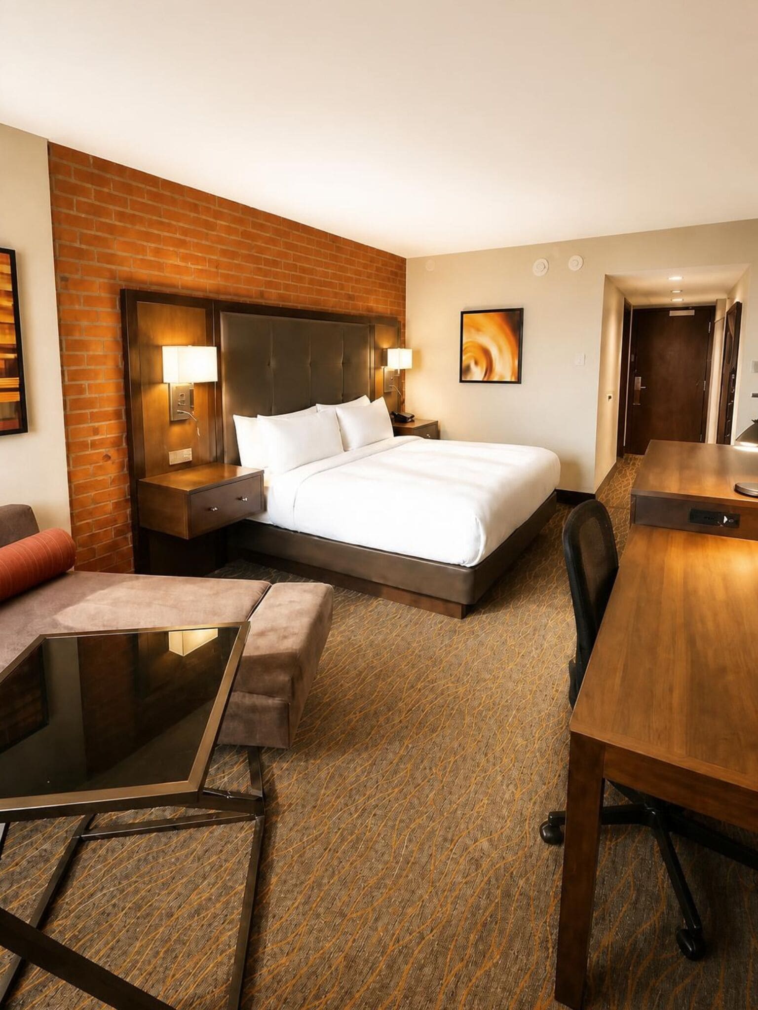 Een hotelkamer met een groot bed, een bureau, een stoel, een kleine tafel en een accentmuur van baksteen.