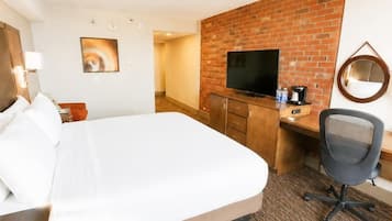 A hotel room with a bed, a desk with a TV, a chair, and a brick wall.