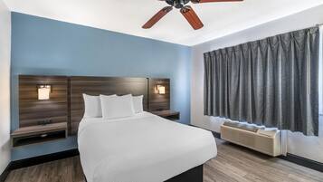Une chambre d’hôtel avec un lit, un ventilateur de plafond, un téléviseur fixé au mur et une fenêtre avec des rideaux.