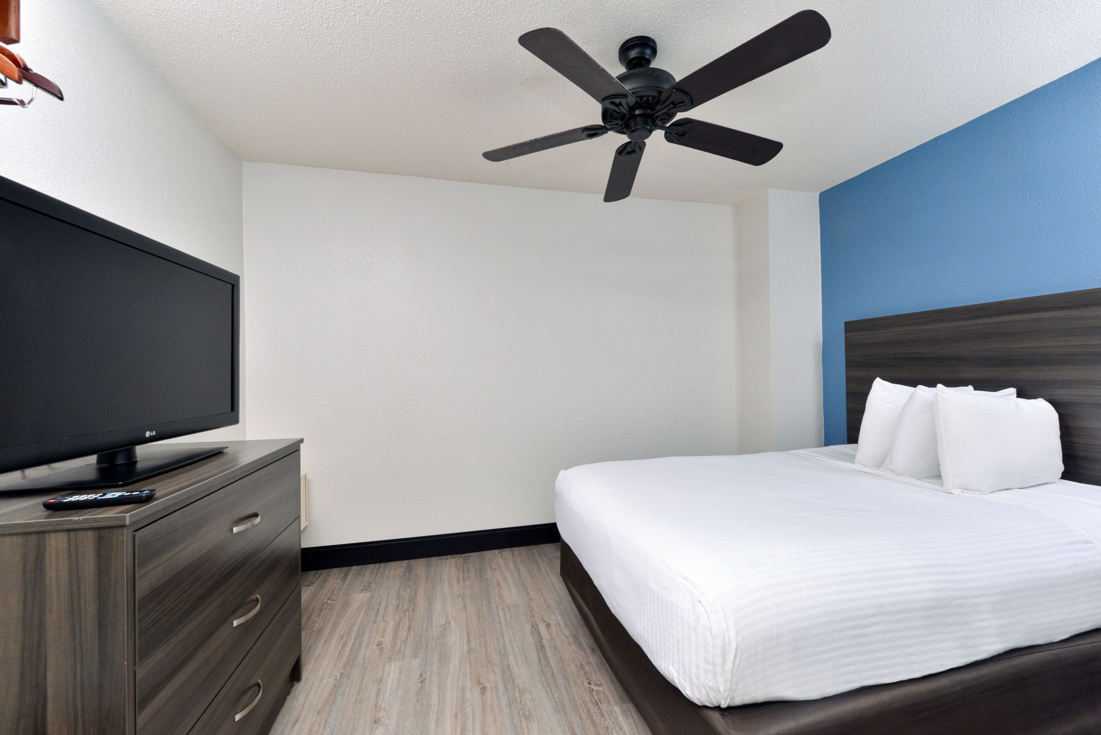 A hotel room with a bed, a TV on a wooden dresser, and a ceiling fan.
