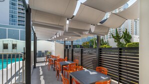 An outdoor seating area with tables and chairs, a pool, and a view of high-rise buildings. - SureStay Hotel by Best Western Virginia Beach Royal Clipper (Virginia Beach)