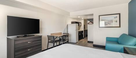 A hotel room with a bed, a TV, a desk with chairs, a kitchenette, and a blue sofa.