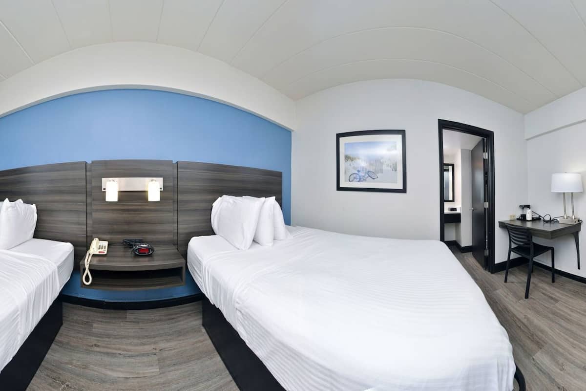 A hotel room with two beds, a desk, a TV, a phone, and a bathroom door.