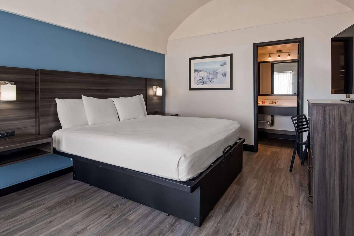 A modern hotel room with a large bed, bedside tables, a desk, and a mirror.
