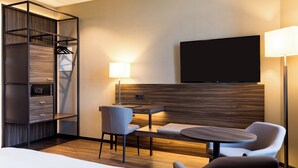 A hotel room with a bed, a desk with a chair, a TV mounted on the wall, and a wardrobe with a mirror. - AC Hotel Mainz (Mainz)