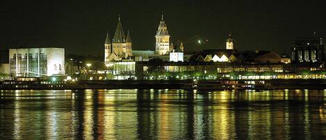 Une vue nocturne d’une ville, avec des bâtiments illuminés dont les reflets se mirent dans l’eau.