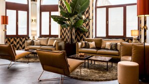 A modern living room with leather sofas, a large plant, and a patterned wall. - AC Hotel Mainz (Mainz)