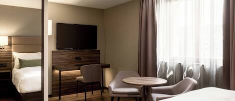 A hotel room with a bed, a desk, a chair, a TV, and a large window with curtains.