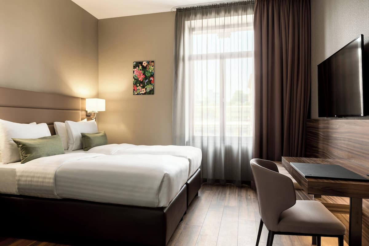 A hotel room with a large bed, a desk, a chair, a TV, and a window with curtains.