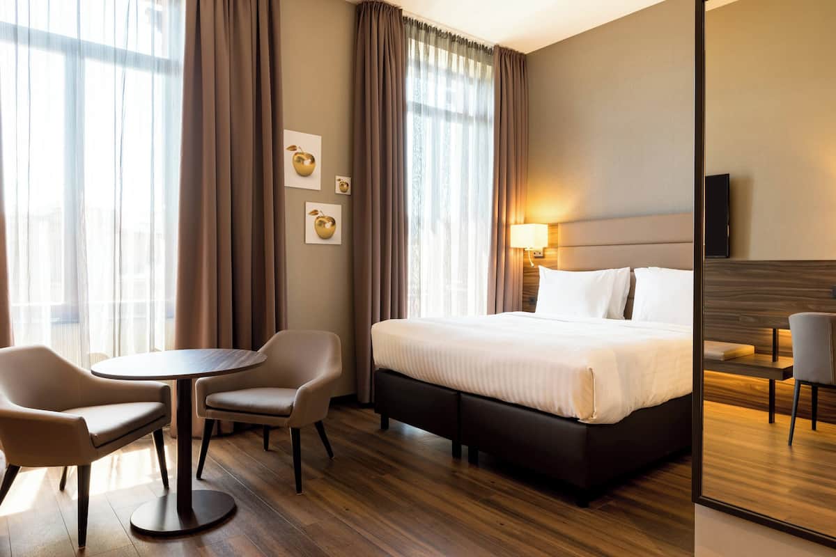 A hotel room with a large bed, two chairs, a small table, and a TV.
