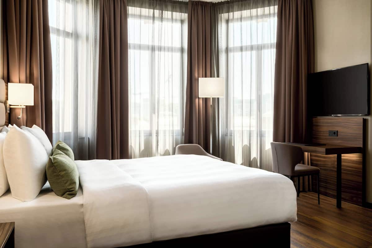 A hotel room with a large bed, a desk, a chair, and a TV.