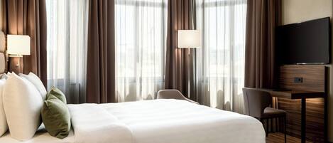 A hotel room with a large bed, a desk, a chair, and a TV.