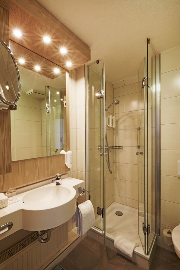 Un baño moderno con ducha de vidrio, lavamanos con espejo e inodoro.
