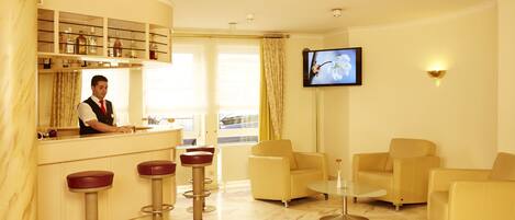Un hall de hotel con barra, zona de estar y televisor.
