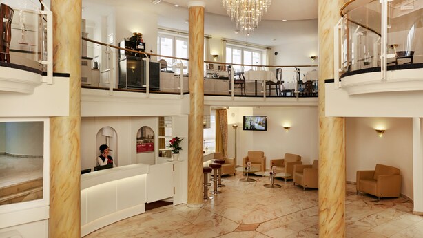 Vestíbulo de hotel con mostrador de recepción, zona de estar y escalera que une dos plantas.