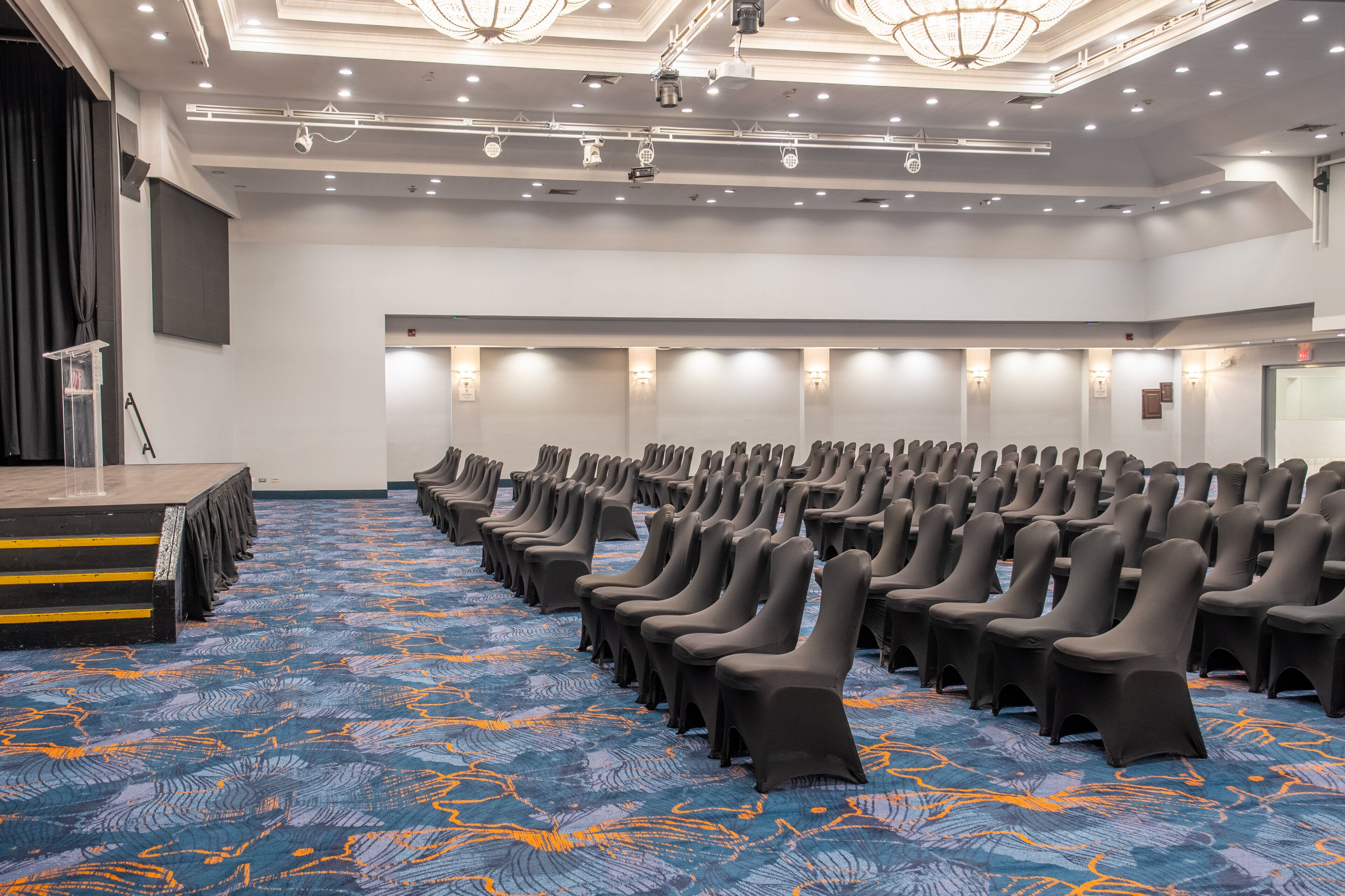 A conference room with rows of chairs, a stage, and a carpeted floor.
