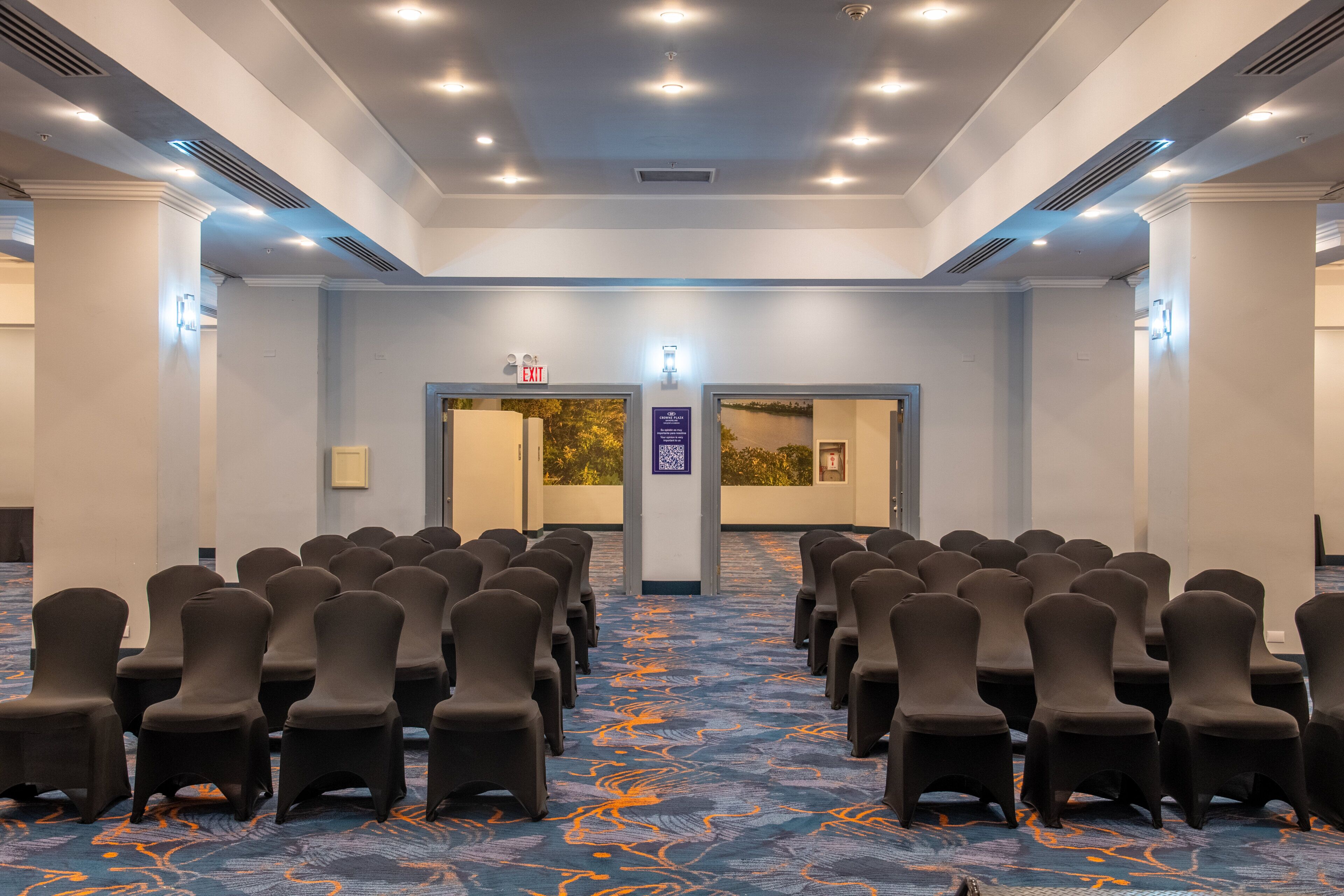Un salón de conferencias con filas de sillas, piso alfombrado e iluminación empotrada en el techo.