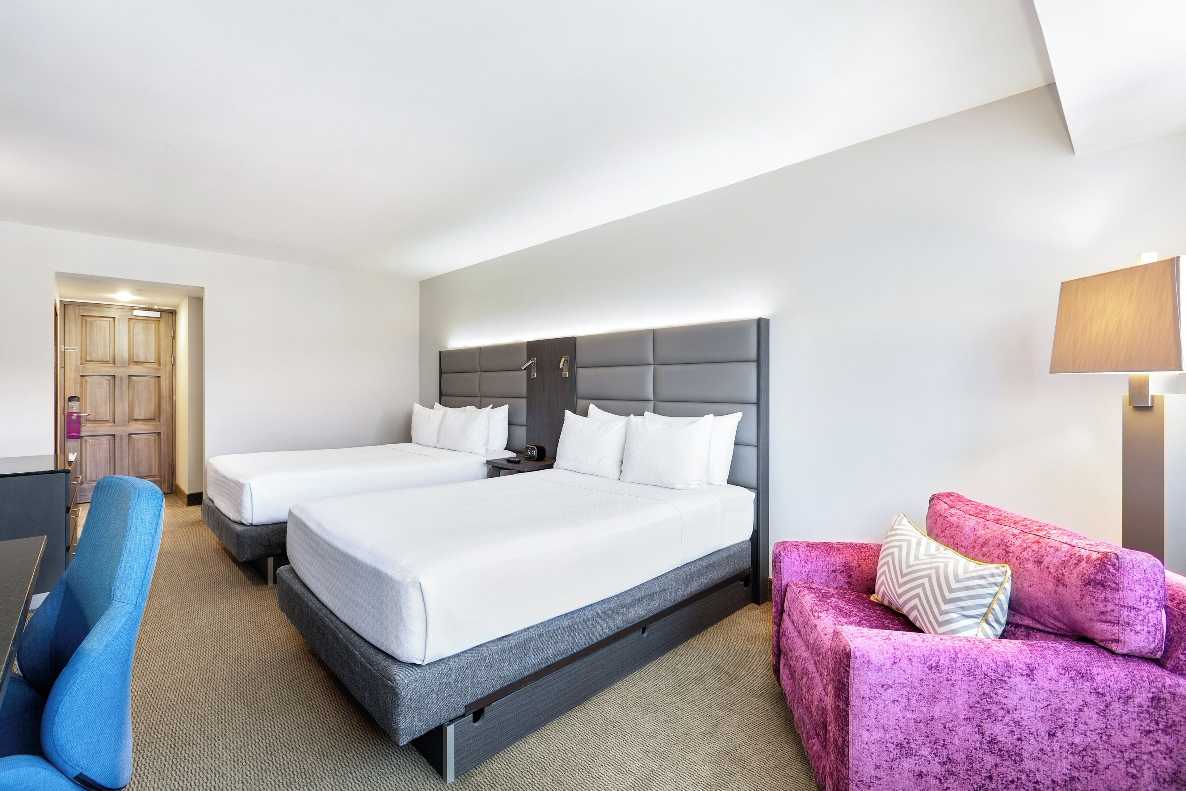 Habitación de hotel con dos camas, un escritorio, una silla, un sofá y una lámpara.