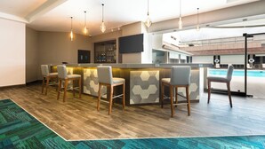 Een moderne bar met houten vloer, barstoelen en hanglampen.