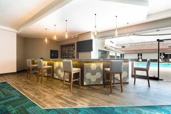 Een moderne bar met houten vloer, barstoelen en hanglampen.