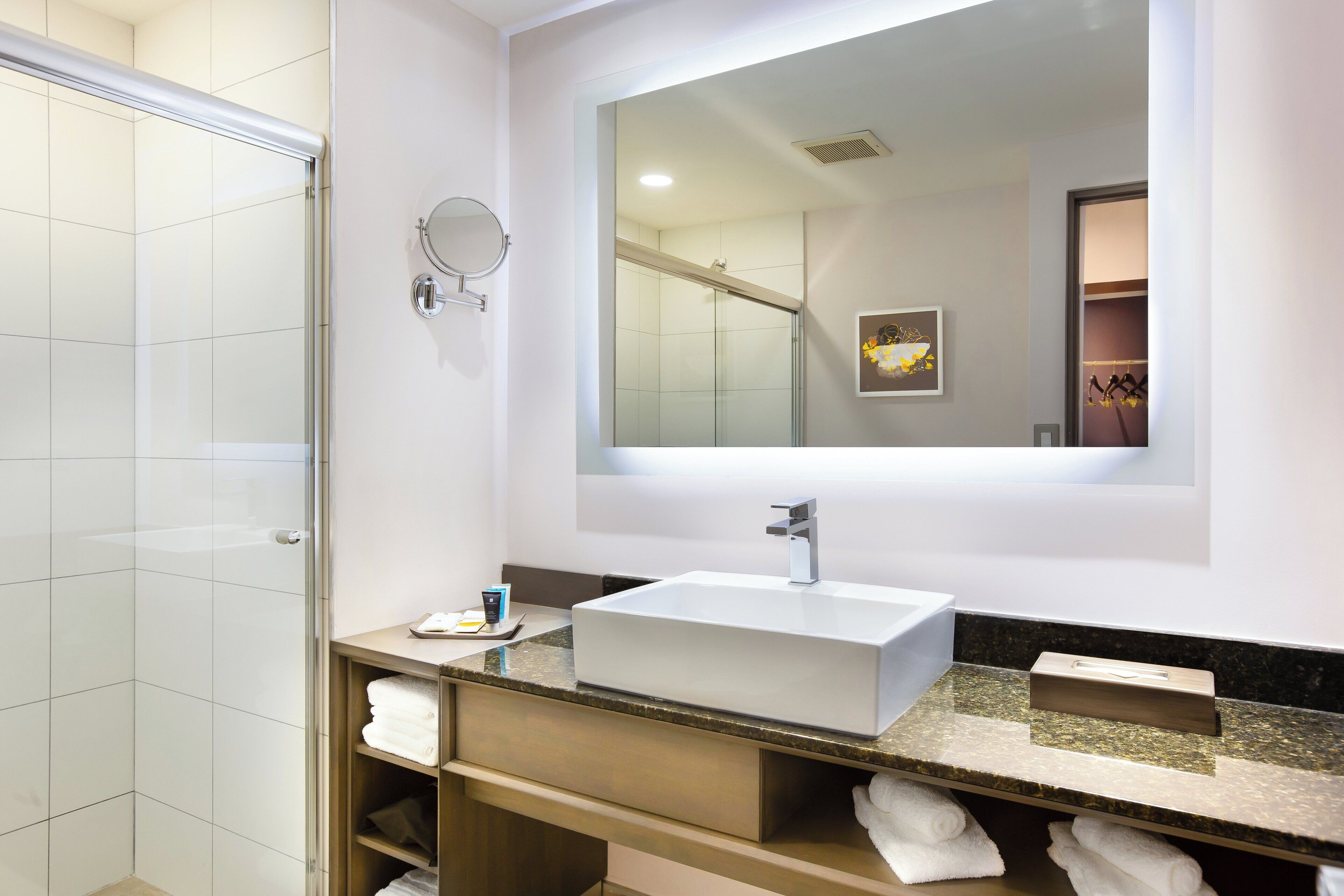 A modern bathroom with a glass shower enclosure, a large mirror, and a white sink with a marble countertop.