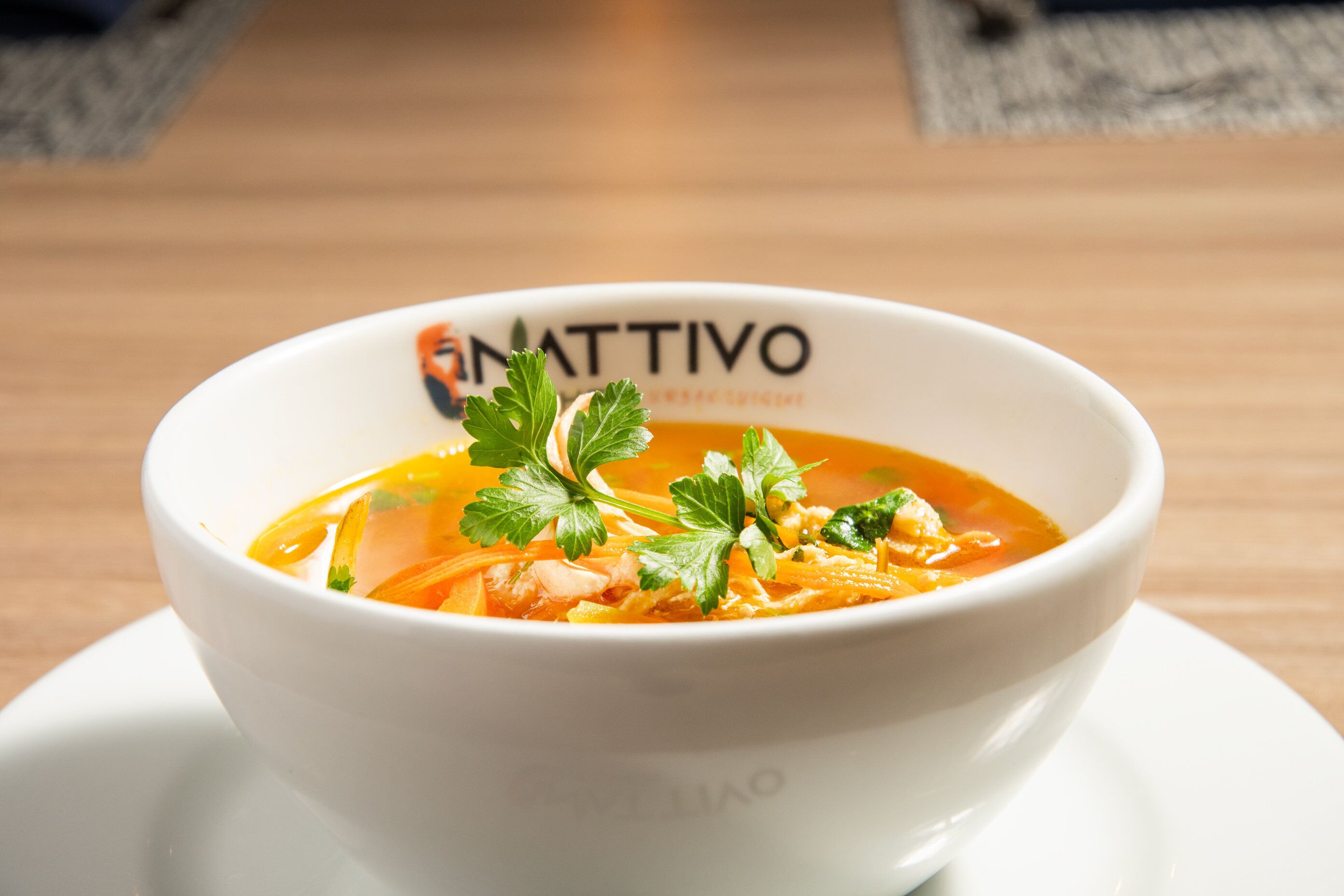 A bowl of soup on a white plate with a logo on the bowl.