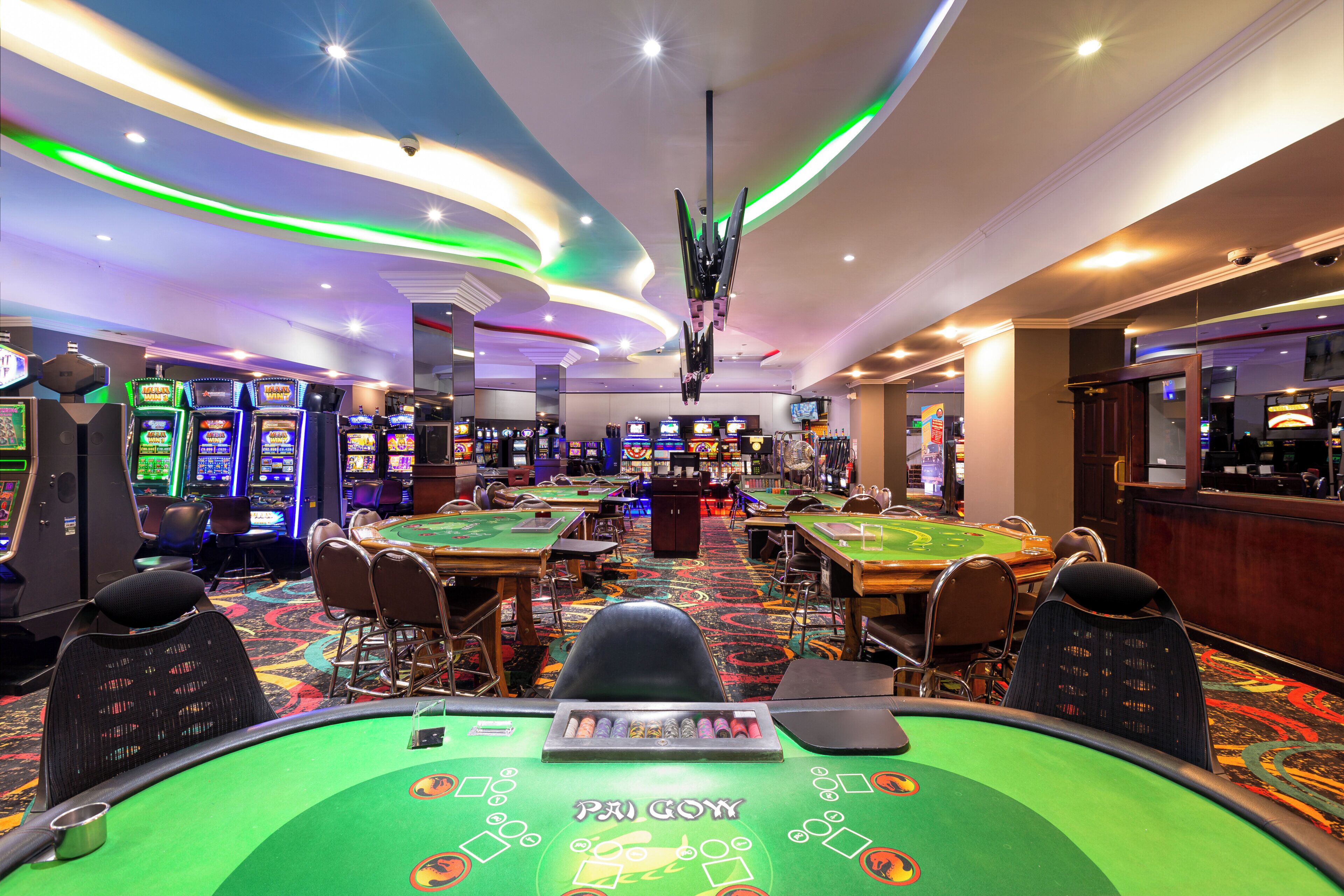 A casino with multiple blackjack tables, slot machines, and a bar area.