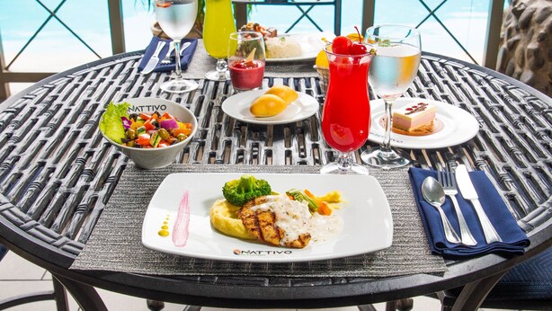 Een eettafel met een maaltijd, inclusief een bord met gegrilde kipfilet, groenten en een portie aardappelpuree. Ook staan er drankjes en een saladeschaal op tafel.