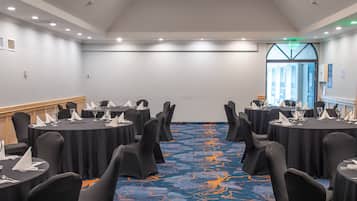 A conference room with round tables, black chairs, and a blue carpet with orange patterns.