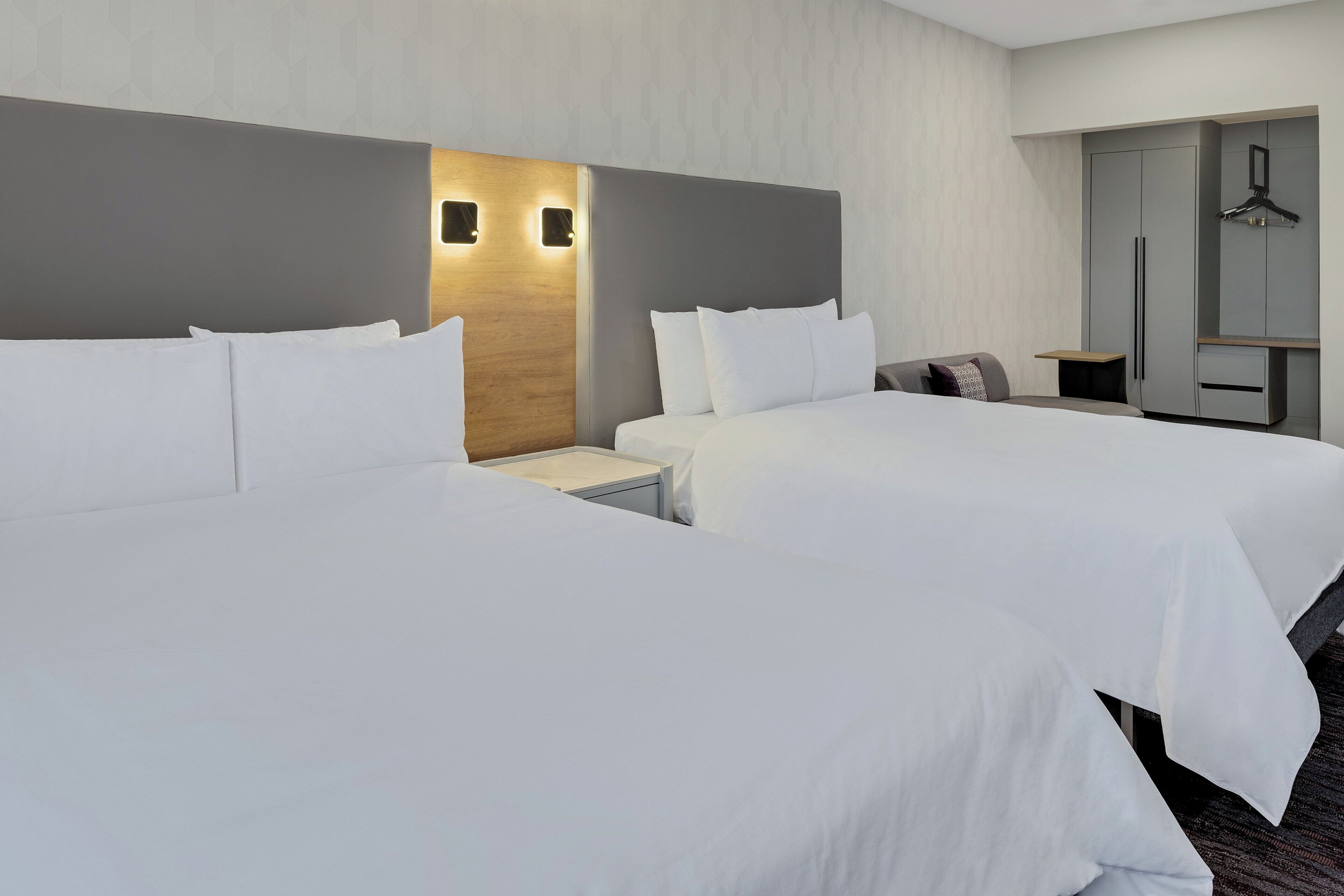 A hotel room with two beds, a wardrobe, and a bedside table.