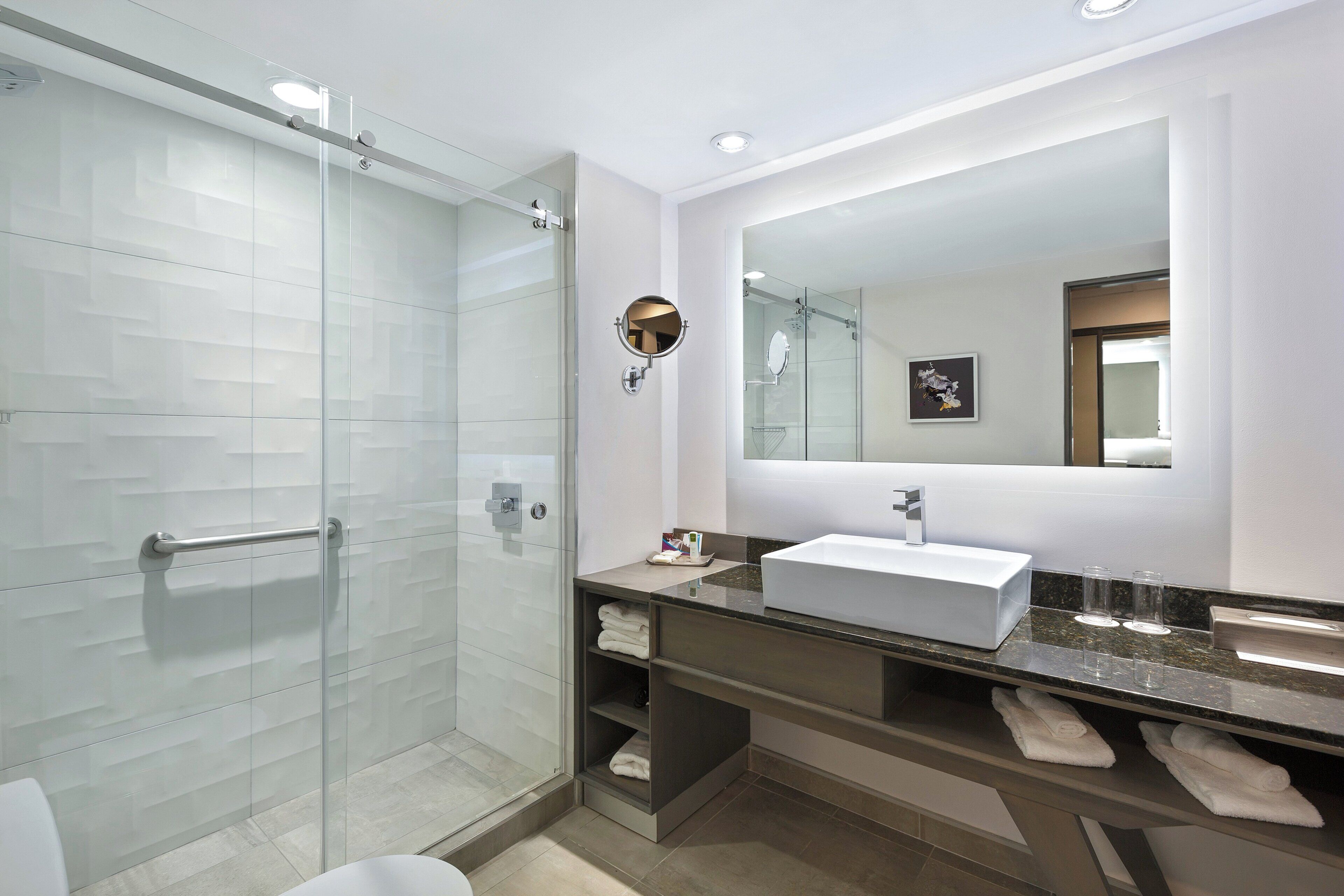 Une salle de bain moderne avec une douche à parois de verre, un grand miroir et un plan de toilette en marbre avec un lavabo.