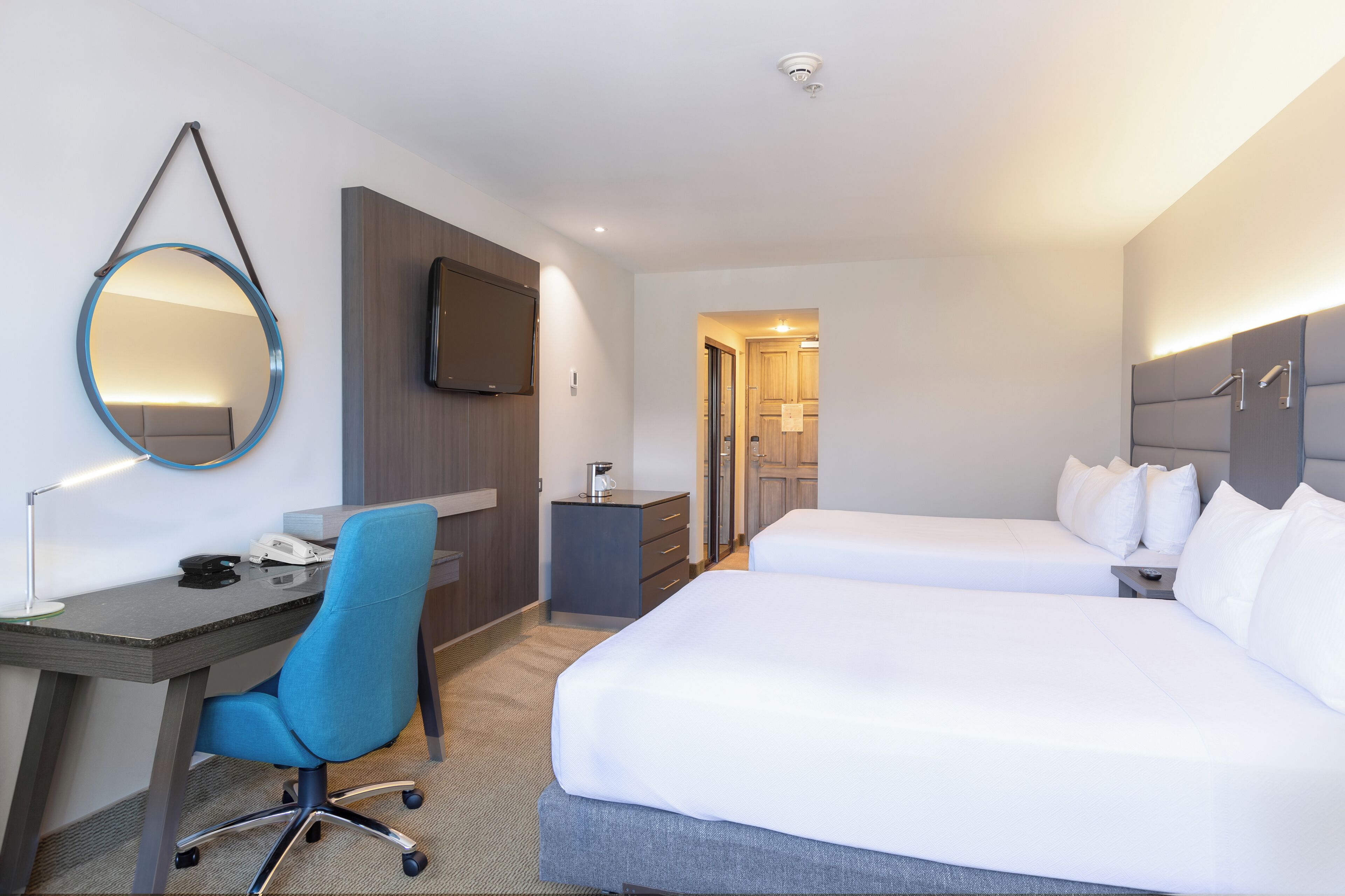 A hotel room with a desk, two beds, a TV, and a mirror.