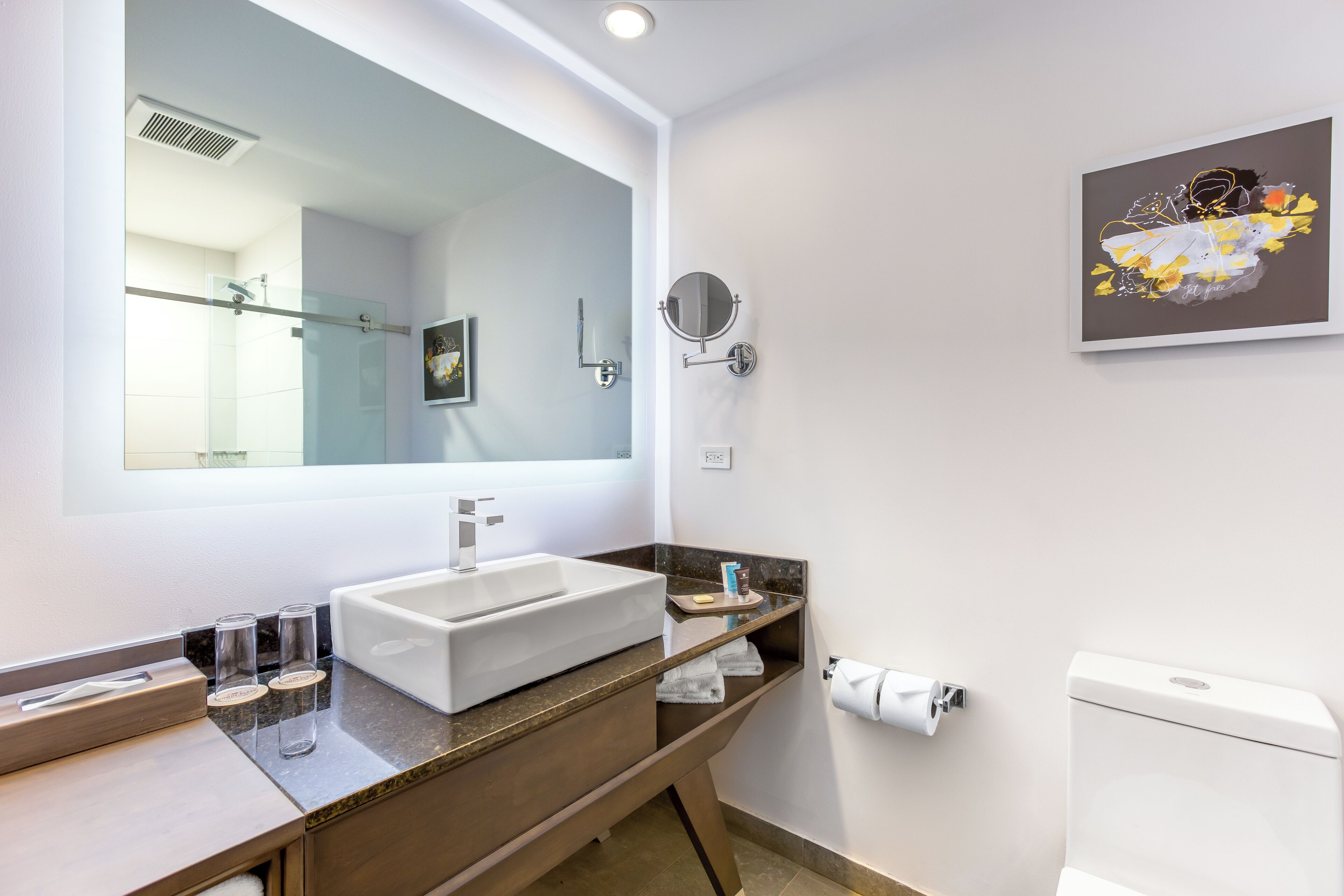 A modern bathroom with a large mirror, a sink, and a toilet.