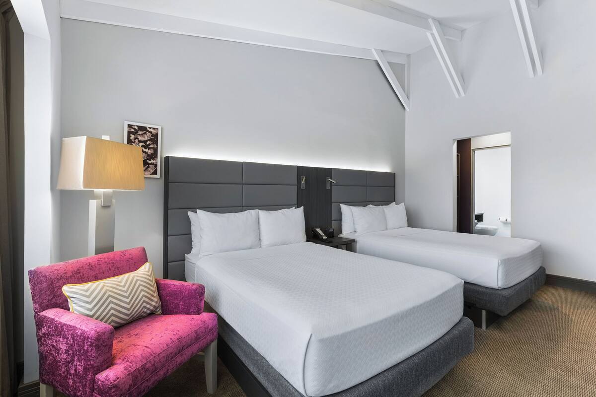 Une chambre d’hôtel avec deux lits, une table de chevet, une lampe, une chaise et un tableau au mur.