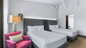 A hotel room with two beds, a nightstand, a lamp, a chair, and a painting on the wall.