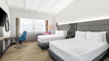 A hotel room with two beds, a desk, a chair, a TV, and a window with curtains.