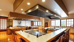 Un restaurante espacioso con una larga barra, sillas de madera y una amplia zona de cocina central.