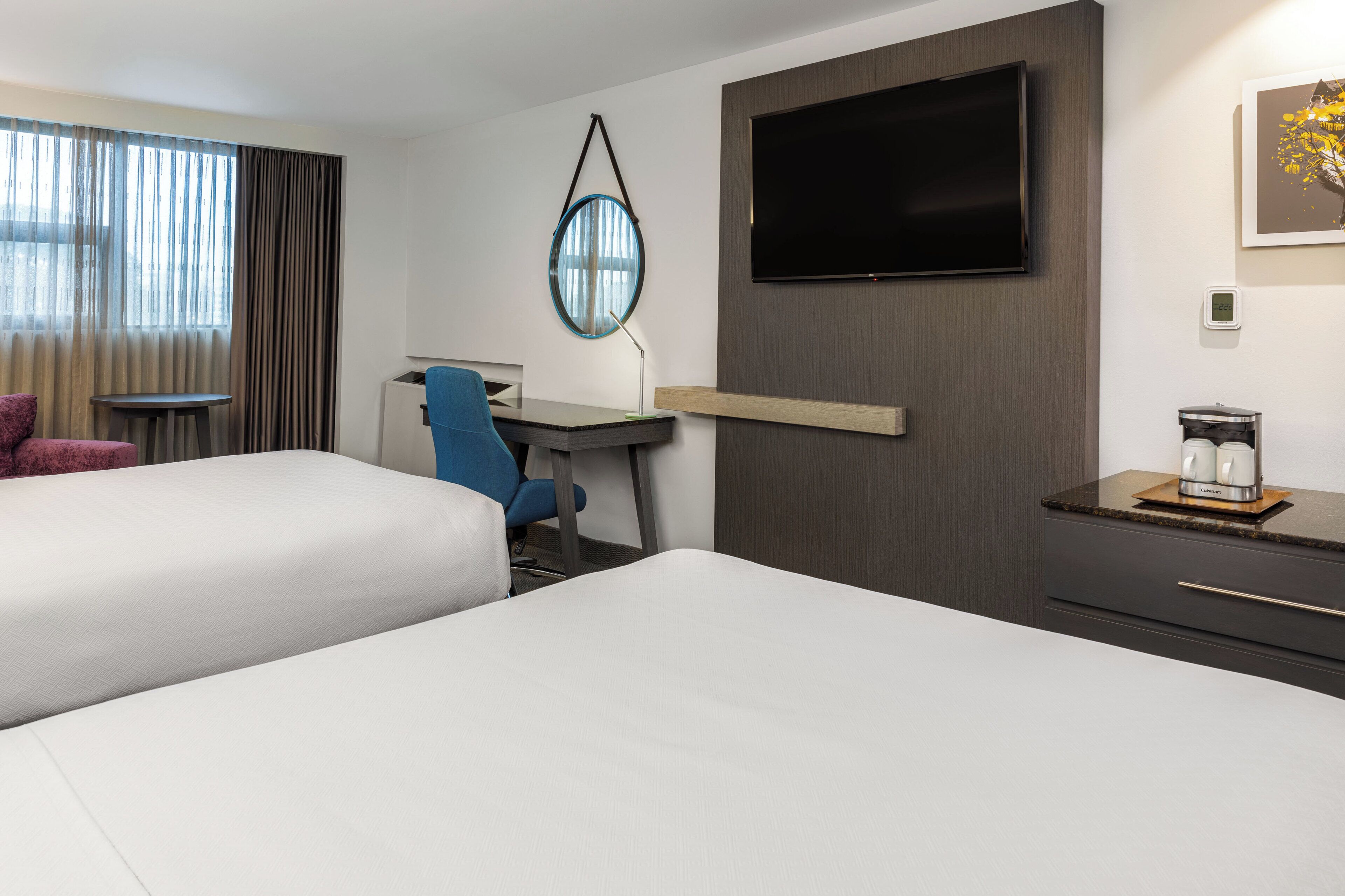 A hotel room with two beds, a desk, a chair, a TV, and a coffee maker.