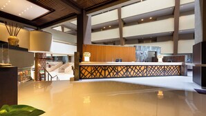 Un moderno vestíbulo de hotel con un mostrador de recepción central, una escalera y una planta grande.