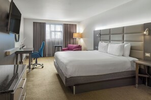 Habitación de hotel con una cama grande, un escritorio con silla, televisión y ventana con cortinas.