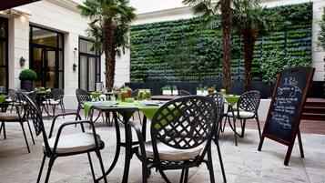 Un'area esterna con tavoli e sedie, un muro verde con piante e un menu alla lavagna.