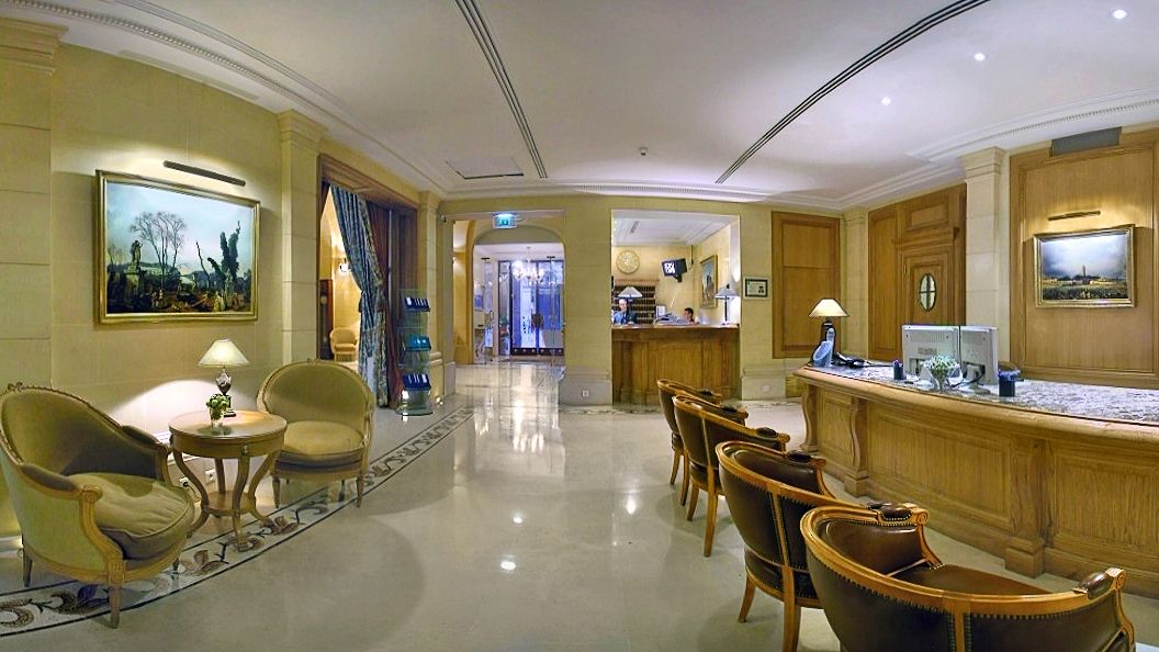 A hotel lobby with a reception desk, seating area with chairs, and a polished floor.