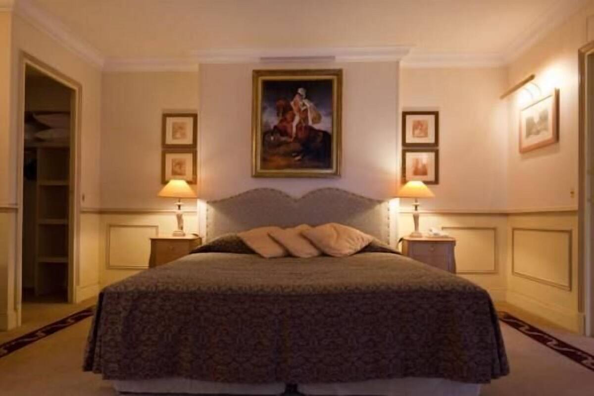 A bedroom with a large bed, two bedside tables with lamps, a painting on the wall, and a door to a closet.