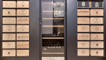 A wine cellar with wooden boxes labeled with names and years, and a glass door reflecting the interior.